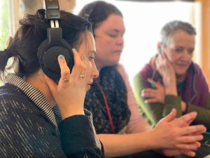 Three women with headphones are listening to something intently.