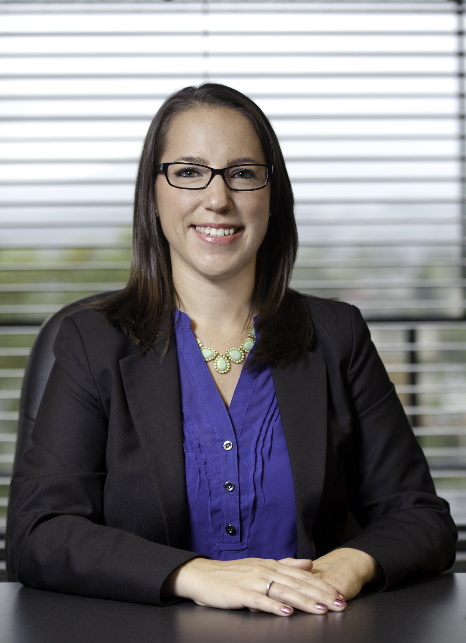 A young woman in business clothes sits at a conference table and smiles.