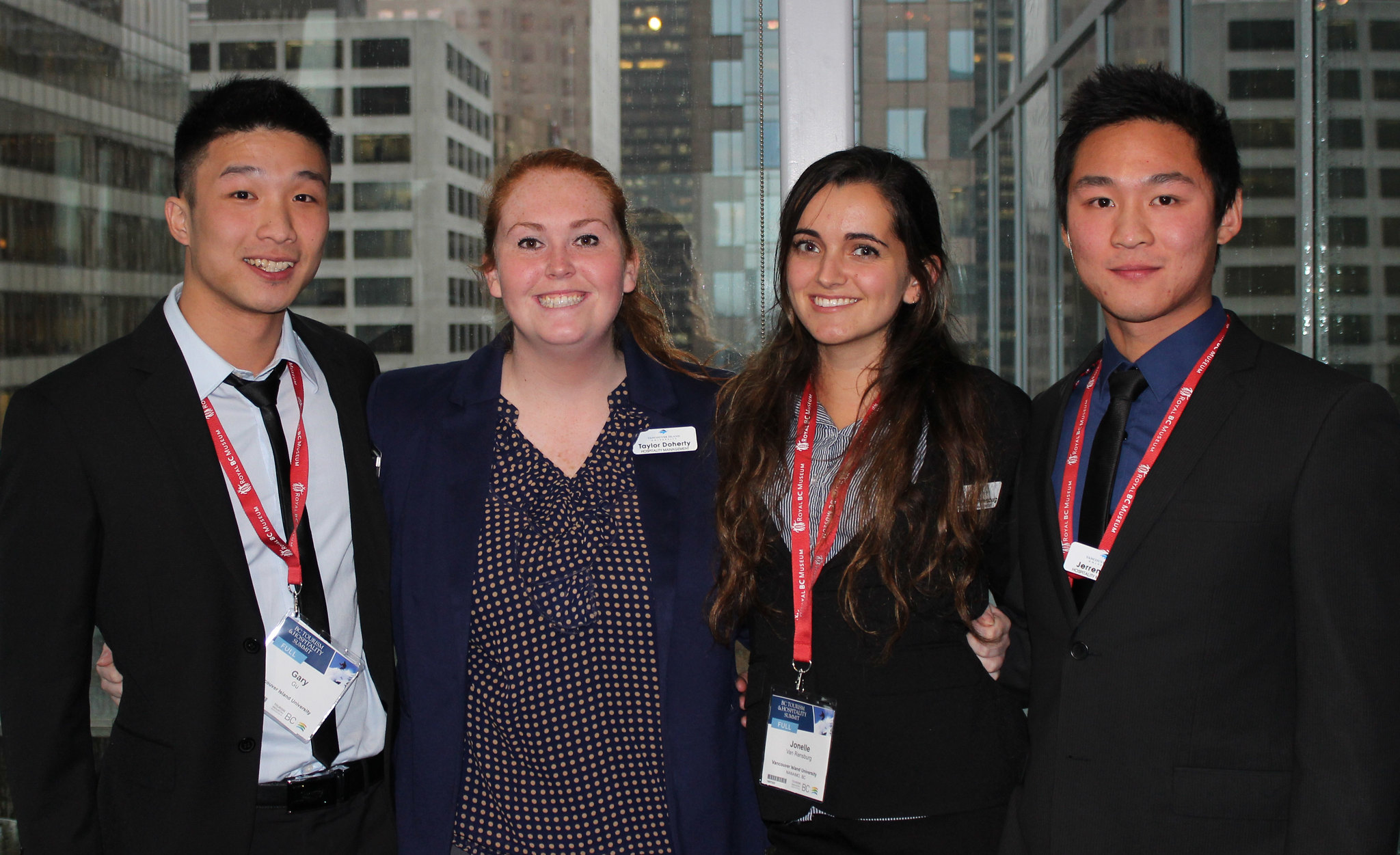 Three students wearing business clothes and lanyards pose with a woman in a blazer.