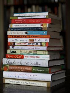 Image of a stack of fiction and non-fiction books ordered from largest to smallest book size of varying colours and format.