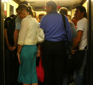 A crowded elevator is shown. There are many people standing close to one another.