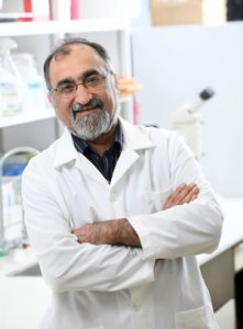 Photograph of Dr. Darvesh wearing a white lab coat with crossed arms, smiling at camera